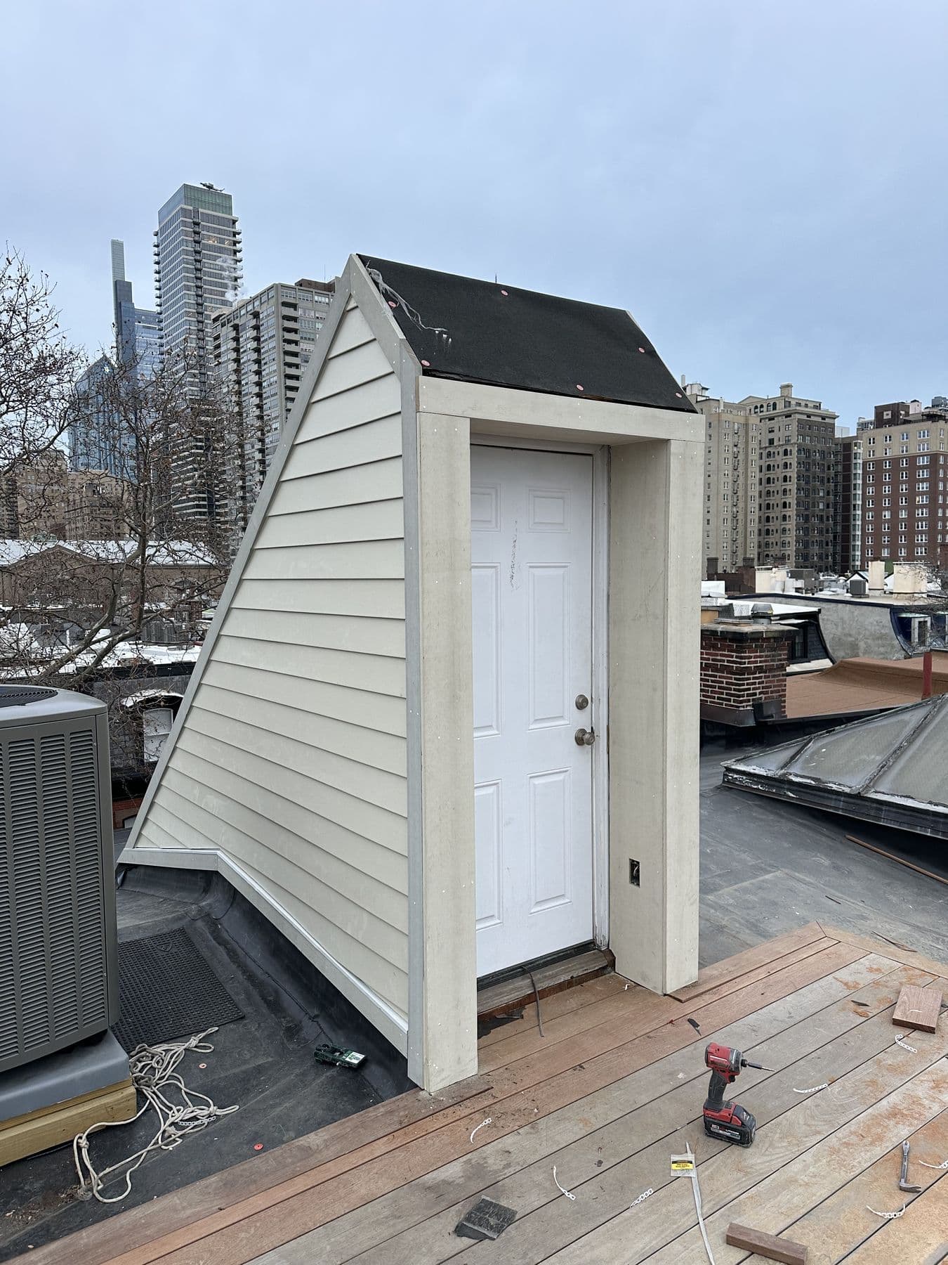 Rooftop stair enclosure with a white door and lap siding, city skyline behind