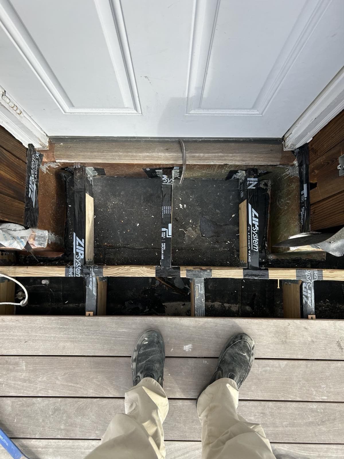Rotted deck framing exposed under removed boards next to a new beam
