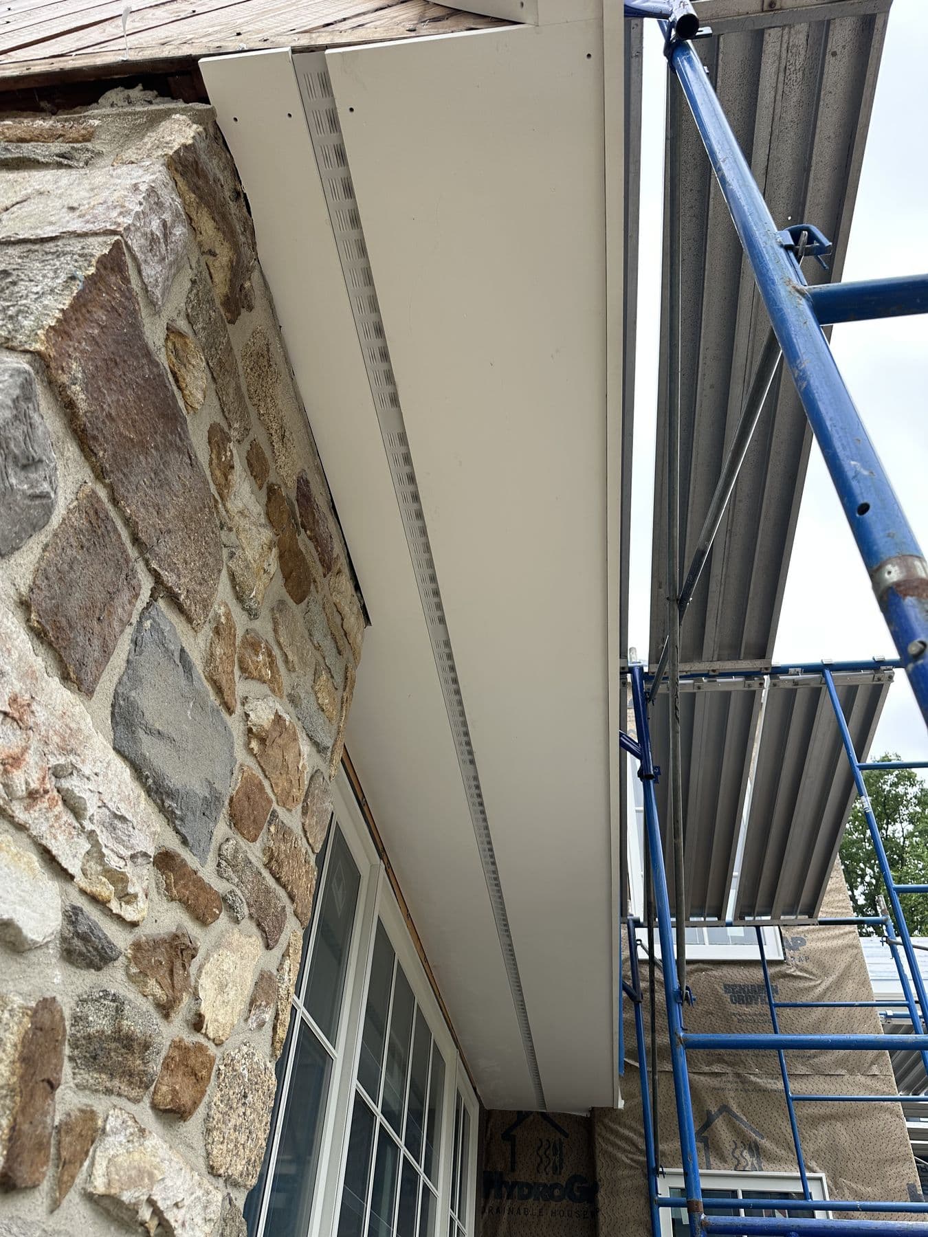 Looking up a fieldstone wall at new white fascia and soffit from the scaffold