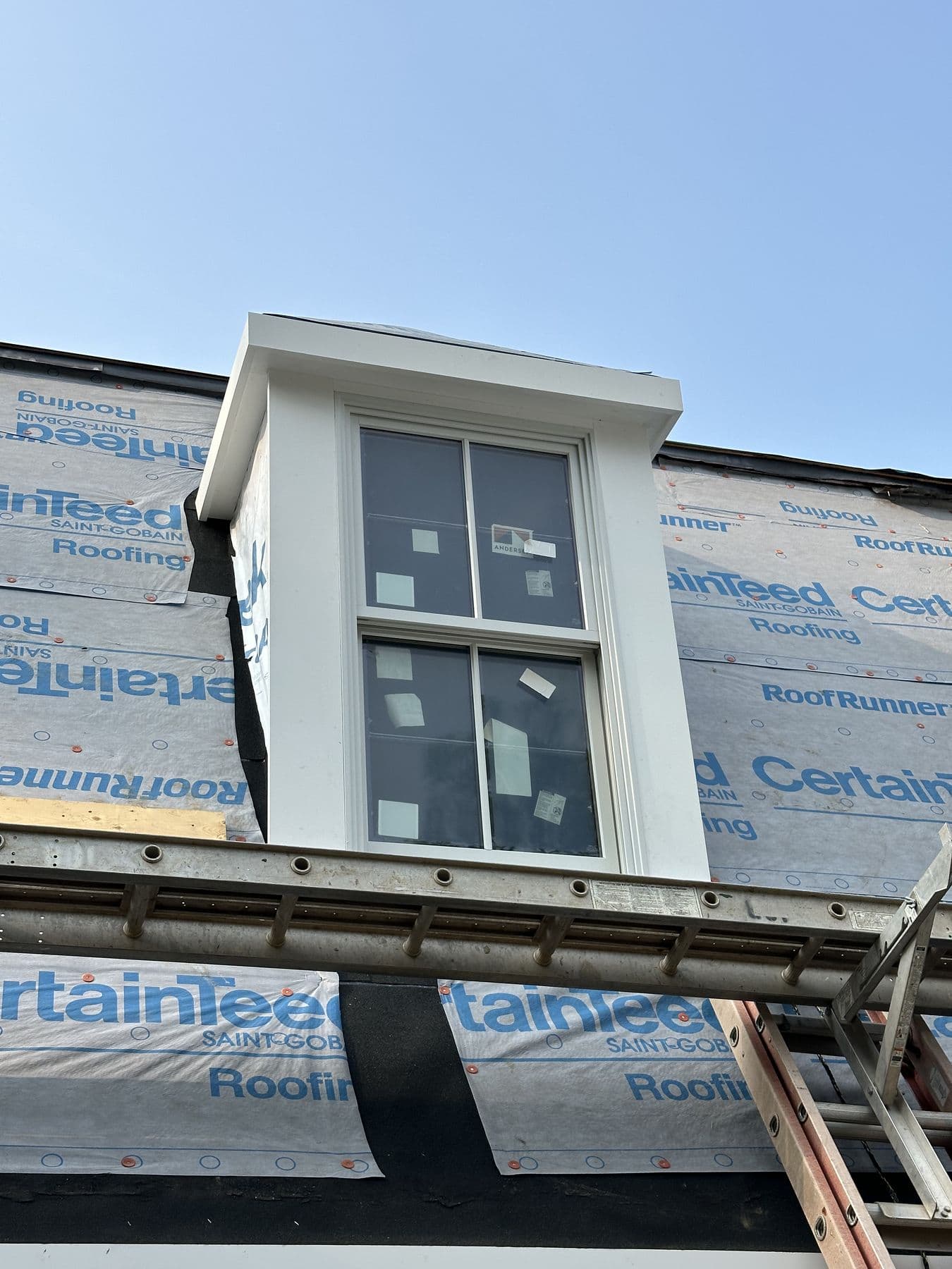 Front of a new dormer with the window installed and white trim going on over the underlayment