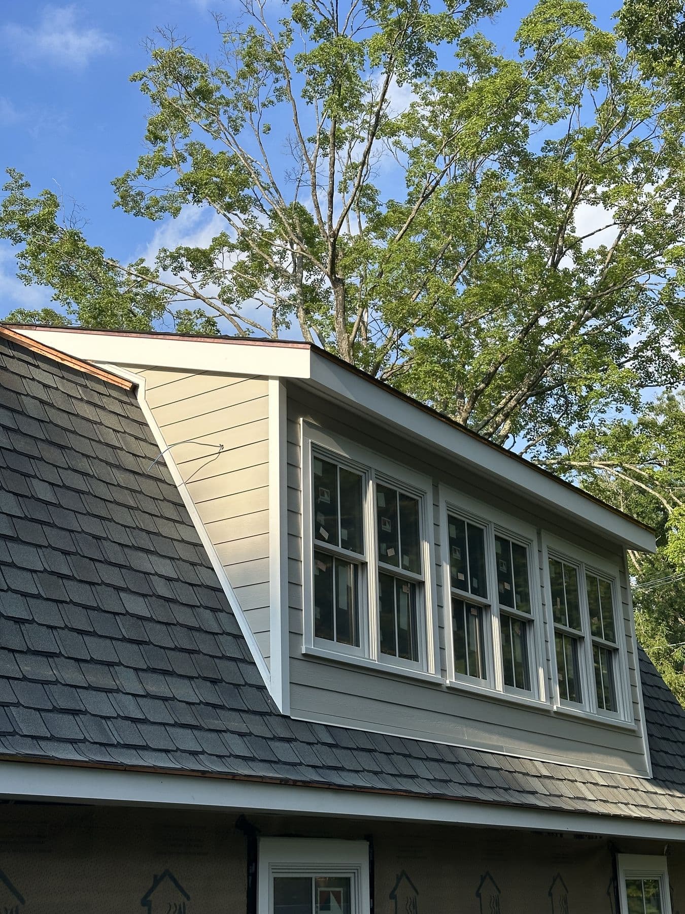Shed dormer with four windows finished in lap siding, white trim and a new shingle roof