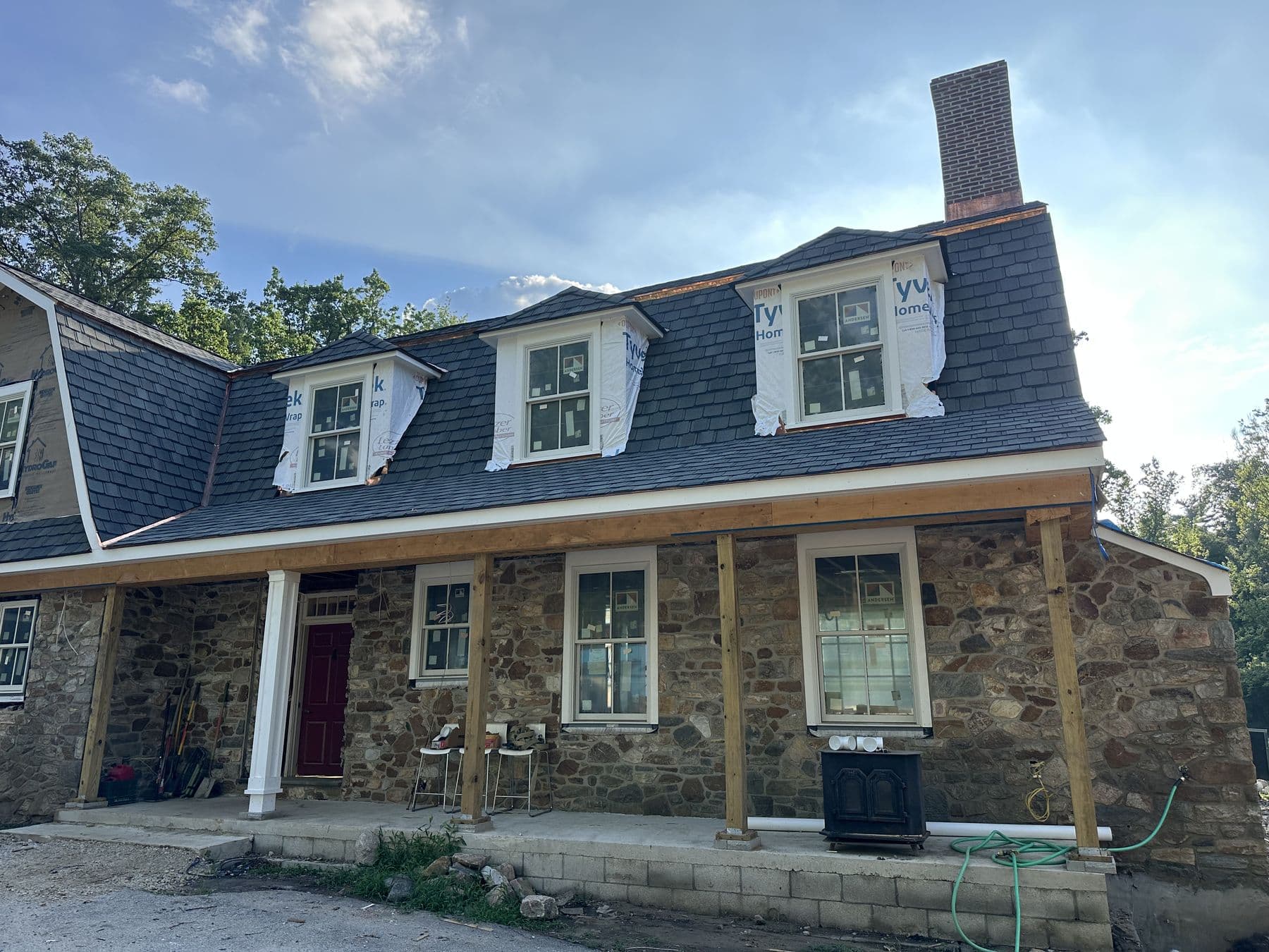 Front of the stone house with a new gambrel roof, three white dormers and a long front porch