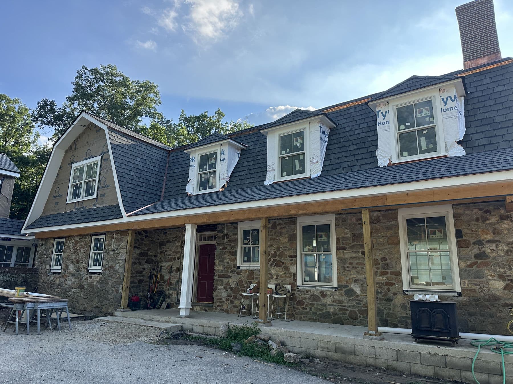 Stone house front with new dormers and the porch roof framed, seen from the drive