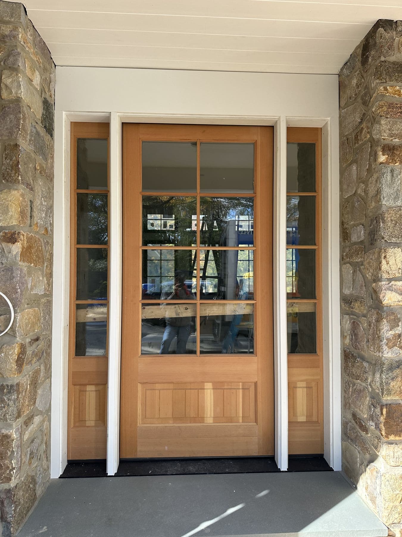 Fir entry door with sidelights set into the fieldstone wall under the porch