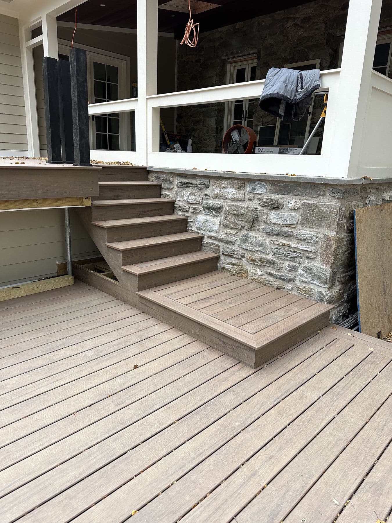 Wide composite landing and steps up to a sunroom, stone wall to the side