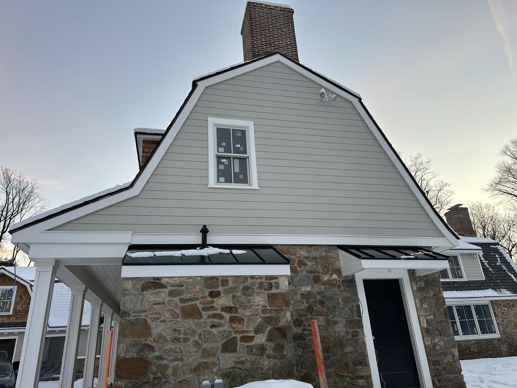 Finished gambrel end in tan lap siding over the stone wall with white trim, winter