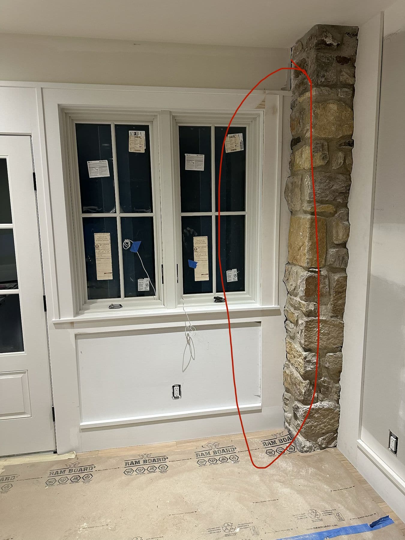 Window and wainscot panel beside an exposed stone column, before paint