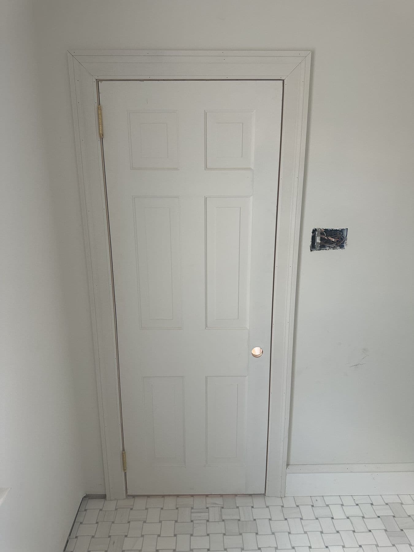 Six-panel door with new casing on a marble basketweave tile floor